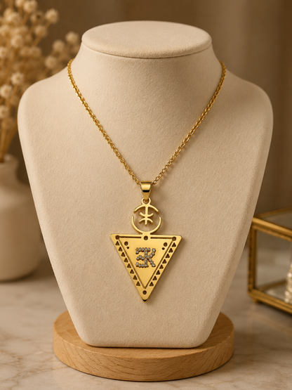 The Collier LALLA is a gold necklace with a large triangular pendant decorated with star, moon, and geometric designs, elegantly displayed on a beige jewelry stand.