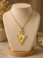 The Collier LALLA is a gold necklace with a large triangular pendant decorated with star, moon, and geometric designs, elegantly displayed on a beige jewelry stand.